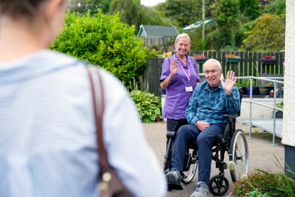 A Hamill Homecare carer and a client waving from the garden outside his home